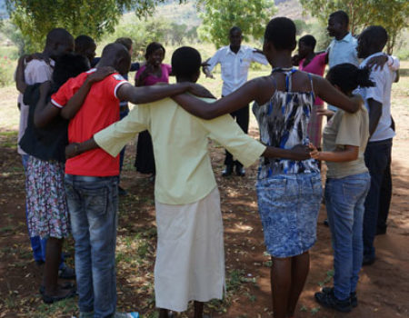 A group of participants in Uganda stand in a circle with arms around one another